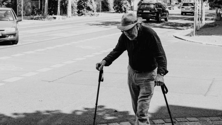 A man with two walking sticks crossing a road.
